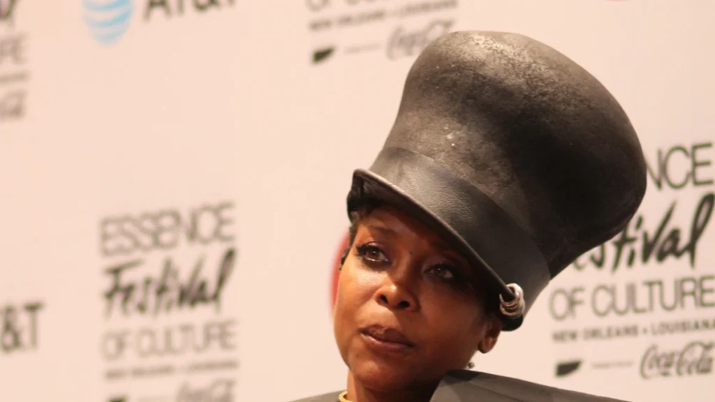 Erykah Badu wearing a tall black hat and holding a microphone at Essence Festival