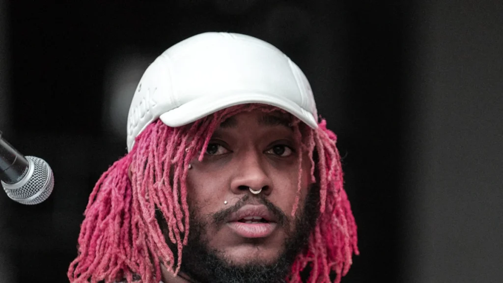 Thundercat holding his bass on stage in a white cap