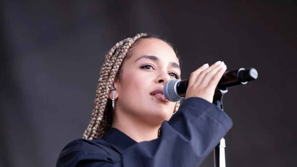 Jorja Smith singing into a microphone on stage at a festival