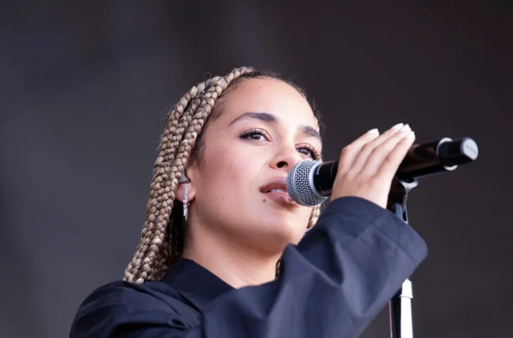 Jorja Smith singing into a microphone on stage at a festival