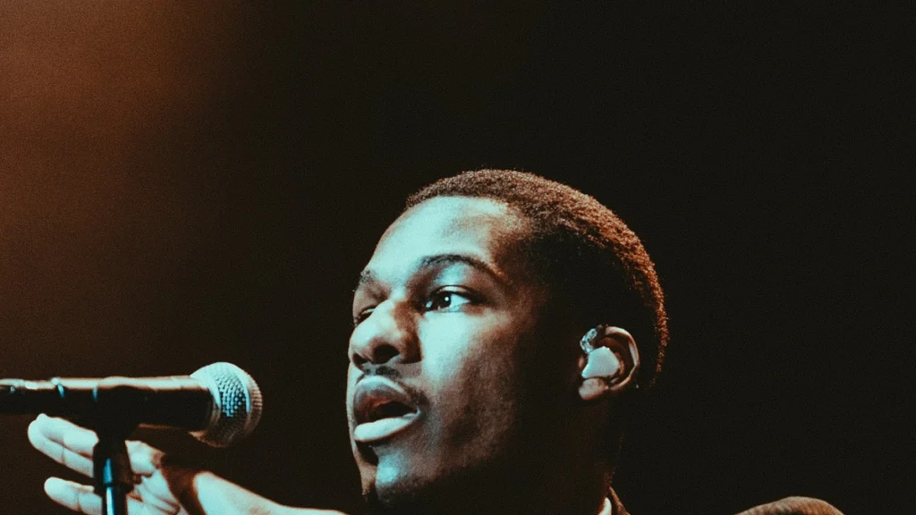 Leon Bridges singing into a microphone under teal stage light