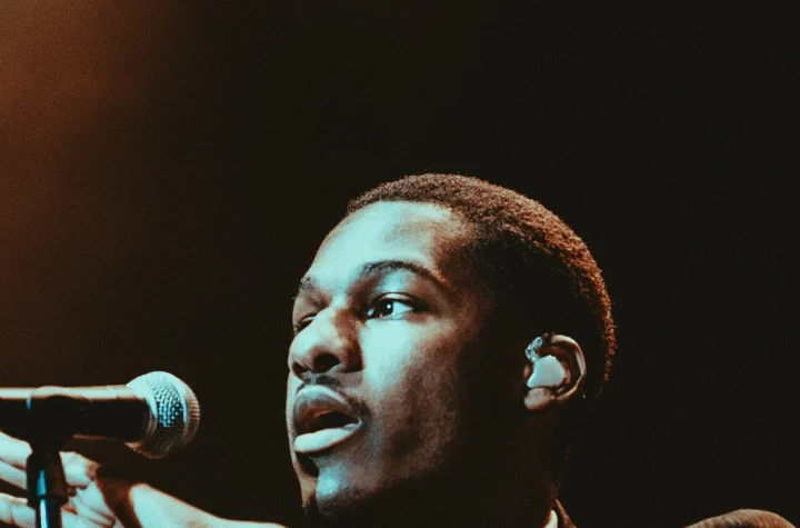 Leon Bridges singing into a microphone under teal stage light