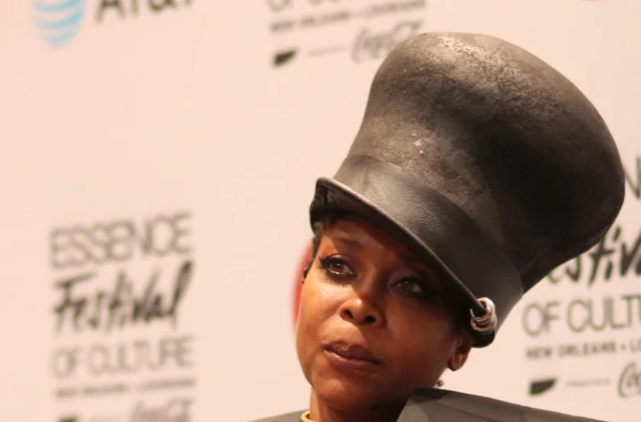 Erykah Badu wearing a tall black hat and holding a microphone at Essence Festival