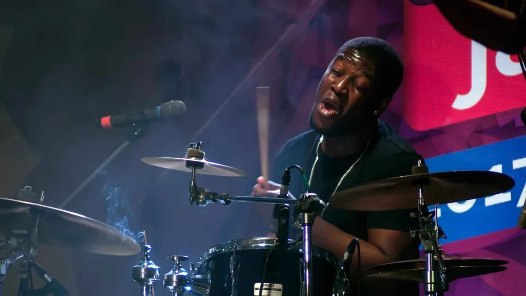 Ezra Collective performing live with the drummer mid-kit under stage lighting
