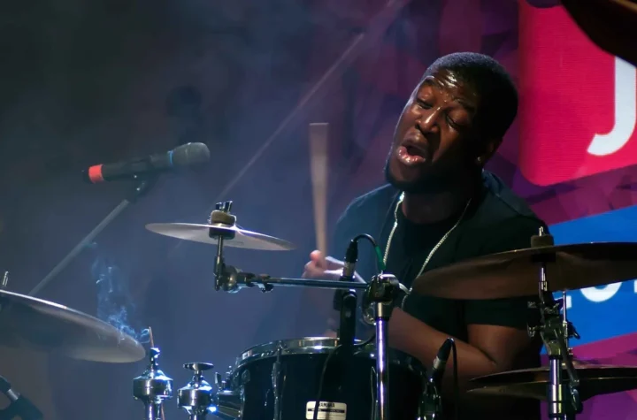 Ezra Collective performing live with the drummer mid-kit under stage lighting